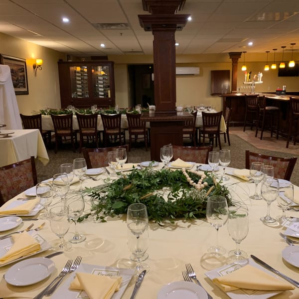 A round table set for dining with wine glasses, plates, and a green wreath centerpiece at Luciano's.