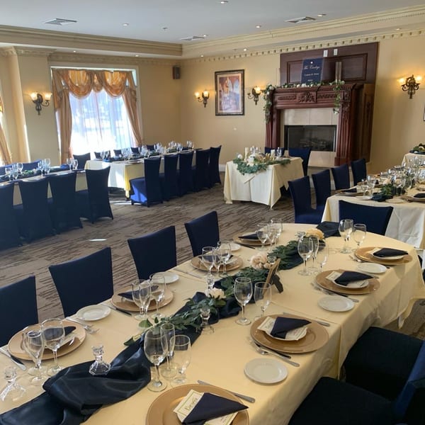Elegant dining room at Luciano's Ristorante with long tables set with gold chargers, blue napkins, and floral centerpieces.