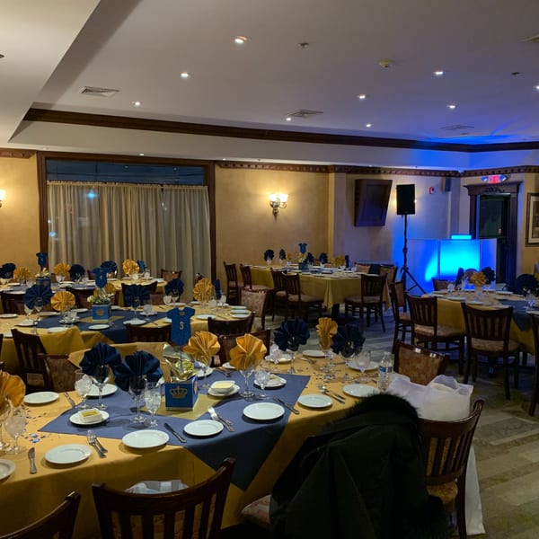 Restaurant dining room set for an event with blue and gold tablecloths, napkins, and centerpieces.