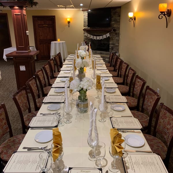 Long dining table set for a banquet with white floral centerpieces and menus at Luciano's Ristorante.