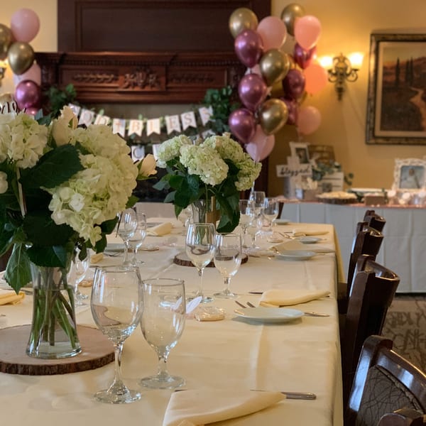 Elegantly set dining table with white hydrangeas, wine glasses, and celebratory balloons at Luciano's Ristorante.