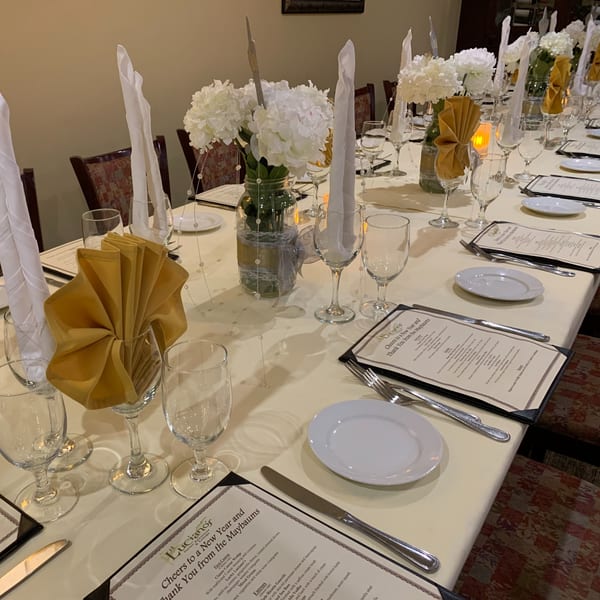 A long dining table at Luciano's Ristorante set with white tablecloths, menus, and floral centerpieces.