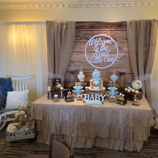 A baby shower dessert table with a "Welcome to the World Little One" sign, cake, and cupcakes.