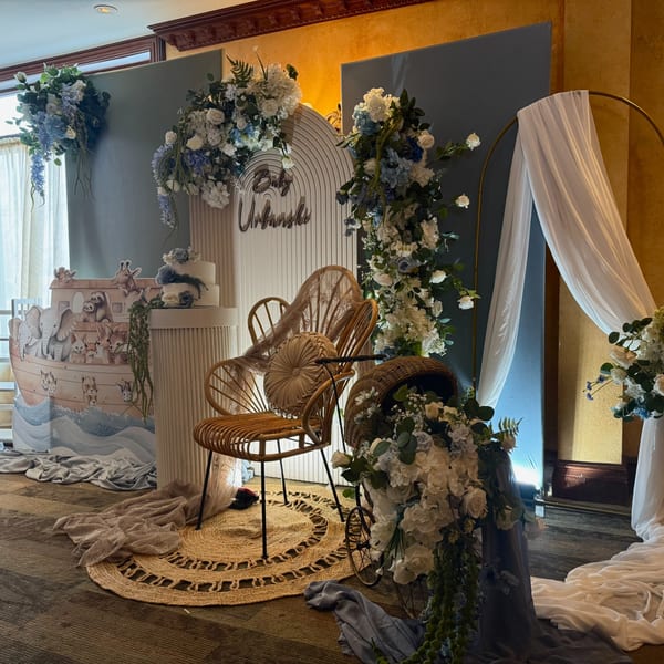 A baby shower setup with blue and white flowers, a Noah's Ark cutout, and a cake.