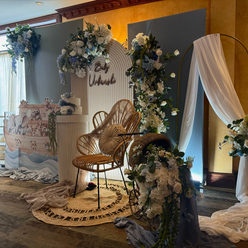 A baby shower setup with blue and white flowers, a Noah's Ark cutout, and a cake.