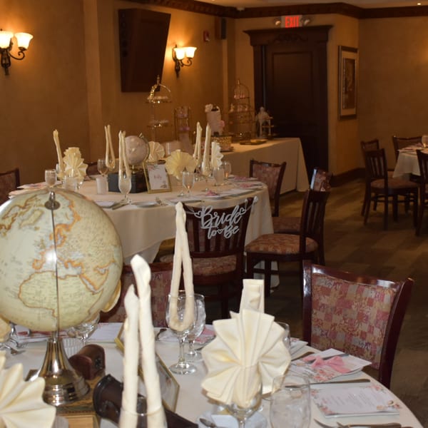 Elegantly set tables with globes, folded napkins, and "Bride to Be" chair decor in a warm-toned dining room.