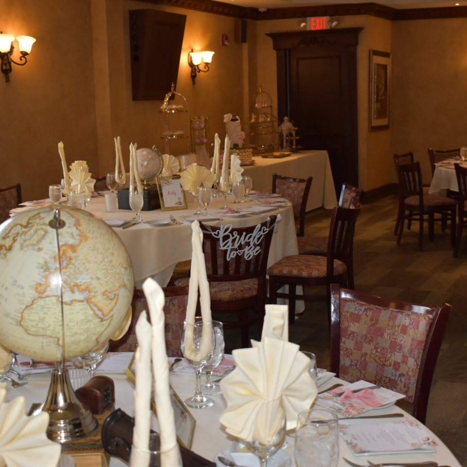 Elegantly set tables with globes, folded napkins, and "Bride to Be" chair decor in a warm-toned dining room.