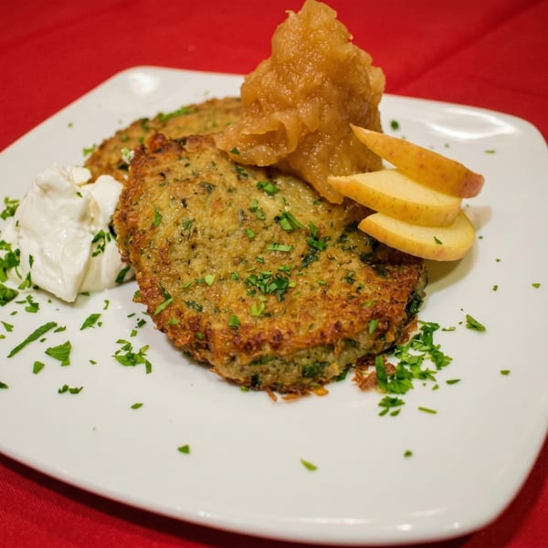 Two golden-brown potato pancakes topped with applesauce, apple slices, and a dollop of sour cream.