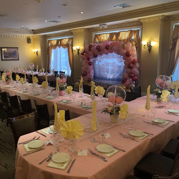 A Luciano's Ristorante dining room set for a party with pink tablecloths, yellow napkins, and balloon decor.