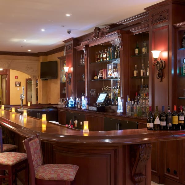 Luciano's Ristorante & Lounge's ornate wooden bar with liquor bottles, wine, and glowing candles.