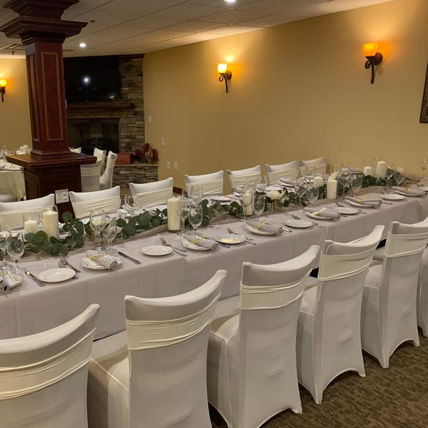 Long dining table set for a banquet with white chairs, candles, and greenery at Luciano's Ristorante.