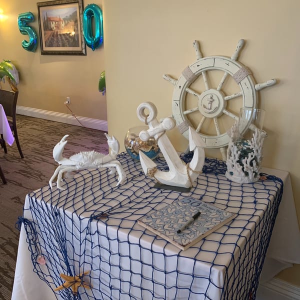 Nautical-themed table decoration with a white crab, anchor, ship's wheel, and blue fishing net.