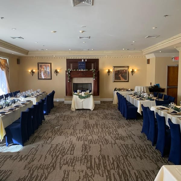 Elegant Luciano's Ristorante dining room with long tables, blue chairs, and a decorated fireplace.