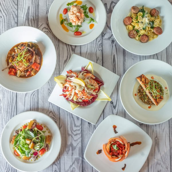 Overhead view of seven Italian dishes, including pasta, salads, seafood, and a pork chop.