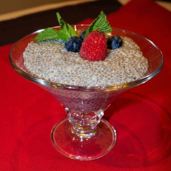 Chia pudding in a martini glass, topped with raspberries, blueberries, and mint leaves on a red tablecloth.