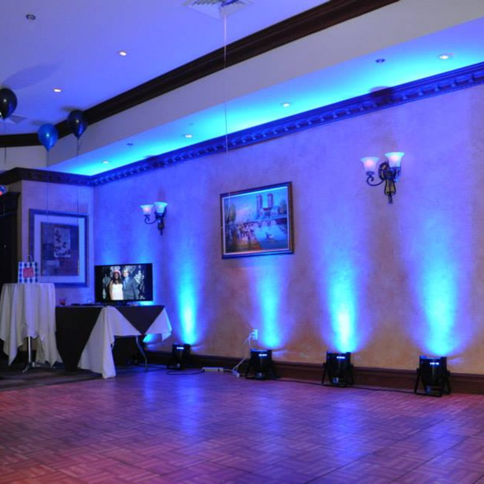 Luciano's Ristorante & Lounge event space with blue uplighting, balloons, and a TV display.