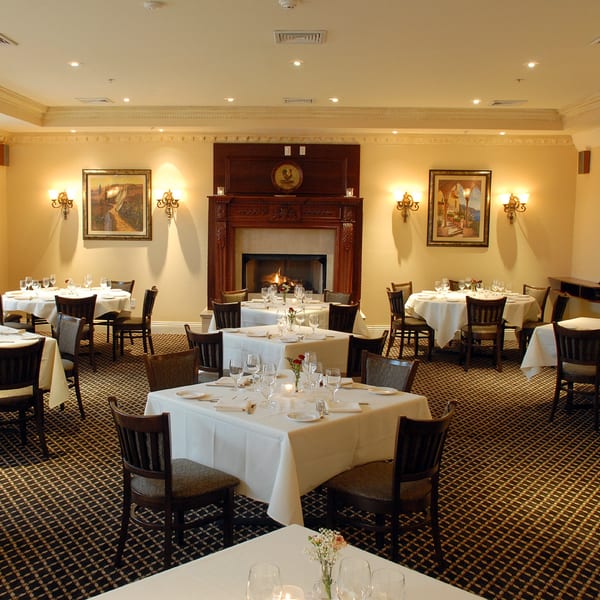 Elegant dining room at Luciano's Ristorante with set tables, a lit fireplace, and warm lighting.