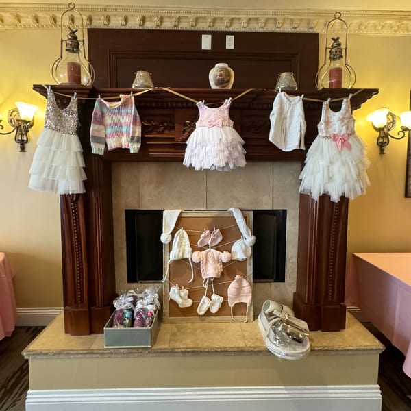 Baby clothes and accessories, including dresses, sweaters, hats, and booties, displayed on a fireplace.
