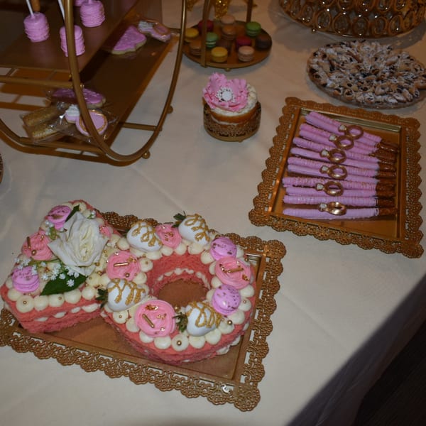 A dessert table with pink and gold themed pastries, including a large number-shaped cake.