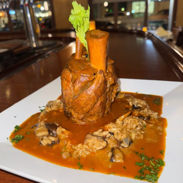 Osso buco with risotto and mushrooms in a rich red sauce, garnished with celery.