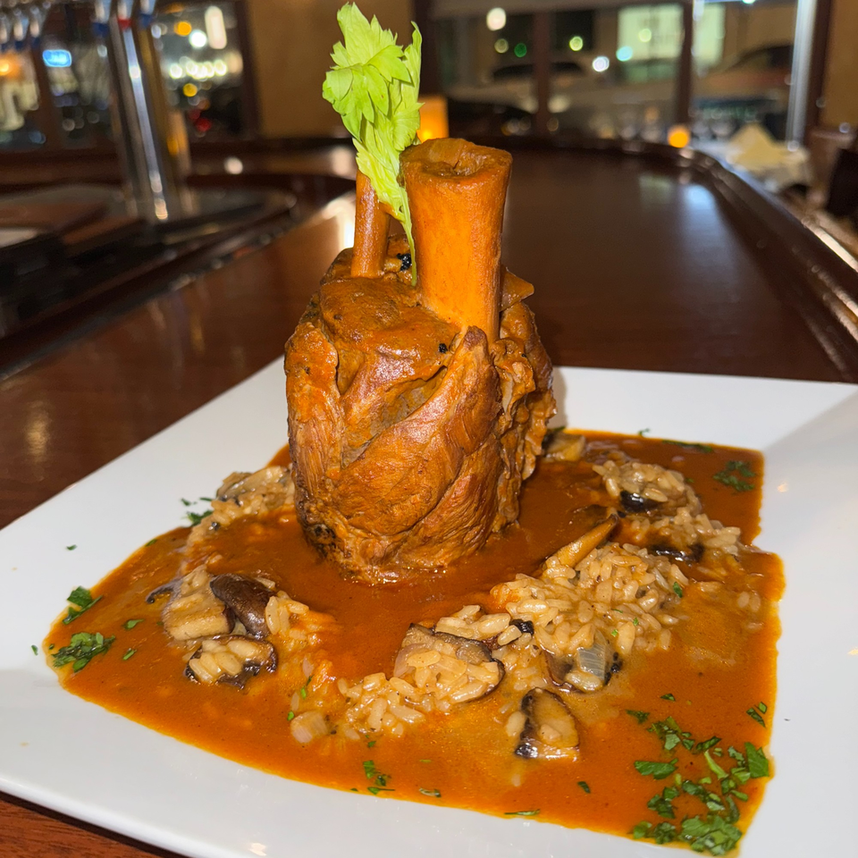 Osso buco with risotto and mushrooms in a rich red sauce, garnished with celery.