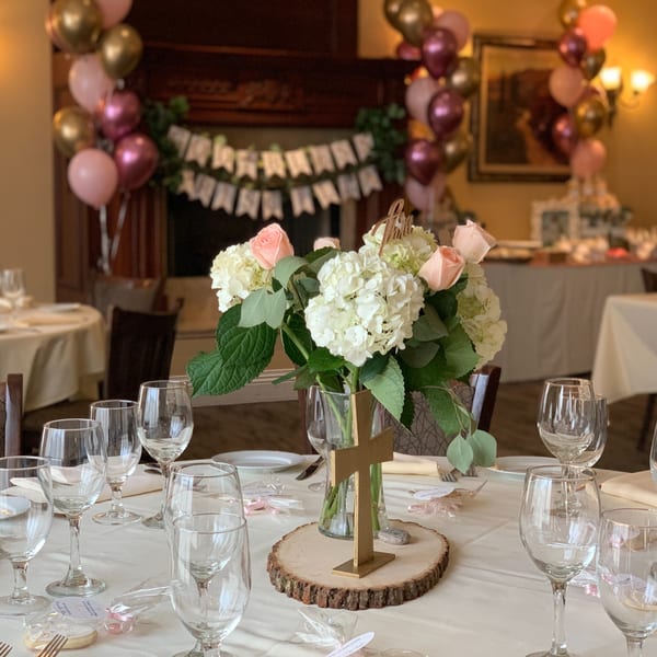 A decorated table with a floral centerpiece, wine glasses, and party favors, with balloons in the background.