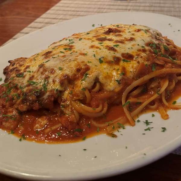 Chicken Parmesan with melted cheese and red sauce over linguine pasta, garnished with parsley.