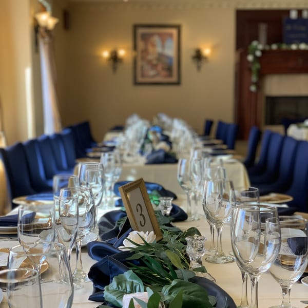 Long dining table set for a banquet with blue chairs, white tablecloths, and elegant place settings.