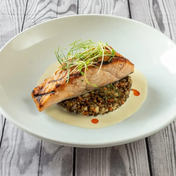 Grilled salmon with lentils, vegetables, and a creamy sauce, garnished with microgreens.